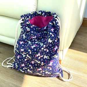 May include: A blue drawstring bag with a pink lining and a unicorn print. The bag has white drawstrings.