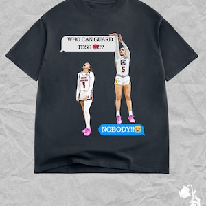 May include: Dark gray t-shirt featuring a basketball player graphic. The graphic includes the text "WHO CAN GUARD TESS?!" and "NOBODY!!" in speech bubbles. The players are wearing white and garnet uniforms.