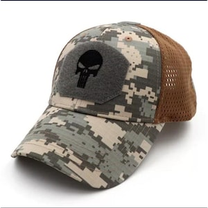 May include: A baseball cap featuring a digital camouflage pattern in shades of green, tan, and grey. The front panel has a grey, pentagonal hook-and-loop patch with a black skull graphic. The back and side panels are made of brown mesh fabric.