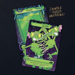 May include: Two rectangular game cards with double-sided artwork featuring a green, two-headed creature with sharp teeth and a skull belt buckle. The cards are labelled Copy and Token, with text stating: This token can be used to represent a copy of something else.