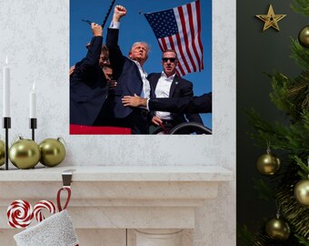 May include: A man in a suit raises his fist in the air while standing on a platform. He is surrounded by other people, including a man in a suit and a woman. An American flag is waving in the background.
