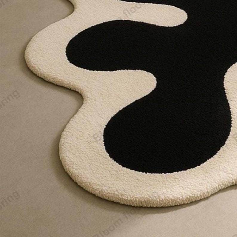Hand-tufted wool rug with black abstract blob on ivory field and a white, wavy edge; bohemian vintage area rug.