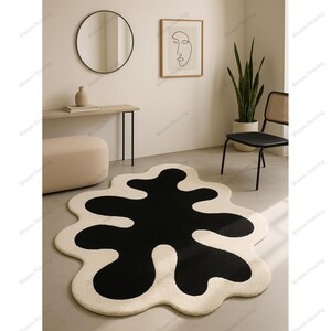 Hand-tufted wool rug with black abstract blob on ivory field and a white, wavy edge; bohemian vintage area rug.