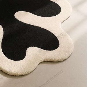 Hand-tufted wool rug with black abstract blob on ivory field and a white, wavy edge; bohemian vintage area rug.