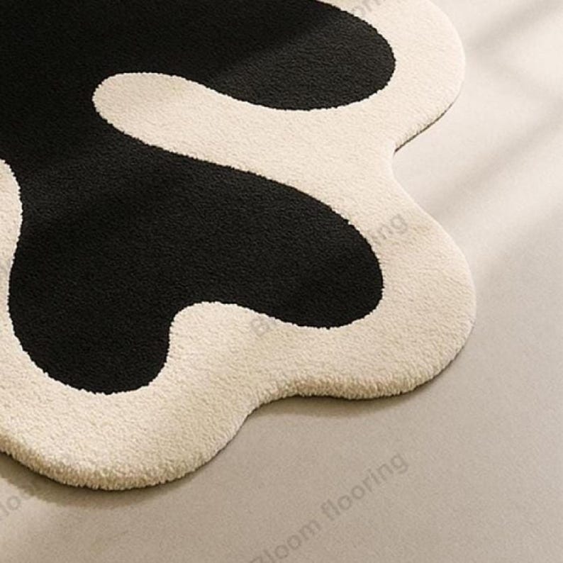 Hand-tufted wool rug with black abstract blob on ivory field and a white, wavy edge; bohemian vintage area rug.