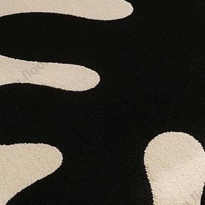Hand-tufted wool rug with black abstract blob on ivory field and a white, wavy edge; bohemian vintage area rug.