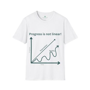 May include: White t-shirt with a green graphic of a line graph showing progress over time. The text "Progress is not linear!" is above the graph. The graph shows two lines, one labeled "Expectation" and the other labeled "Reality".