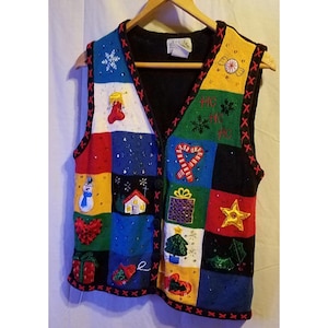 May include: A colorful Christmas-themed sweater vest with a patchwork design. The vest features various holiday-themed appliqués, including a snowman, snowflakes, and candy canes. The vest is sleeveless with a V-neck and is displayed on a wooden hanger.