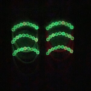 May include: Two glow-in-the-dark bracelets with the name "Elizabeth" spelled out in green beads with pink accents.