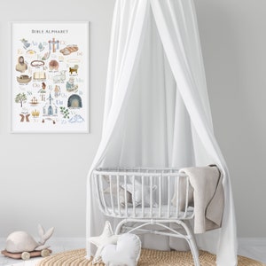 May include: A white crib canopy with a white wicker crib and a white and beige blanket. A white and beige stuffed animal is on the floor in front of the crib. A framed print with the text "Bible Alphabet" is on the wall behind the crib. The print features a watercolor illustration of the alphabet with images related to the Bible.