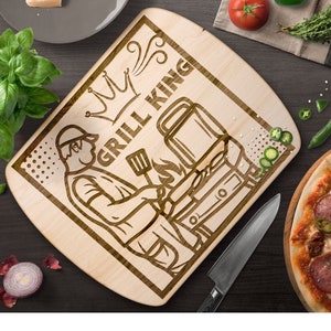 May include: A wooden chopping board with a laser-engraved design of a person grilling with the text "Grill King" and a crown above the text.