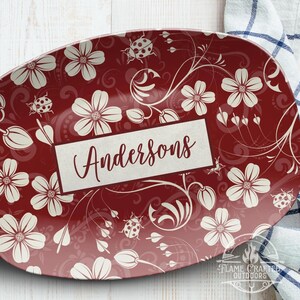 Könnte beinhalten: Eine bordeauxfarbene Servierplatte mit Blumen- und Marienkäfer-Design. Die Platte zeigt weiße Blumen, Ranken und Marienkäfer. Der Name "Andersons" wird in einem rechteckigen Feld in der Mitte der Platte angezeigt.