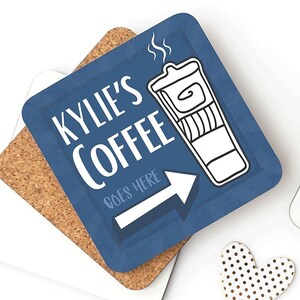 Könnte beinhalten: Quadratischer blauer Untersetzer mit dem Text "KYLIE'S COFFEE" und einer Kaffeetassen-Illustration. Ein weißer Pfeil zeigt nach rechts, darunter die Worte "GOES HERE". Der Untersetzer liegt auf einem Korkuntersetzer.