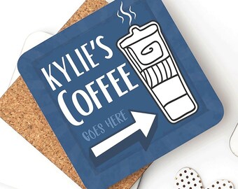 Puede incluir: Posavasos cuadrado azul con el texto "KYLIE'S COFFEE" y una ilustración de una taza de café. Una flecha blanca apunta hacia la derecha, con las palabras "GOES HERE" debajo. El posavasos está sobre un posavasos de corcho.