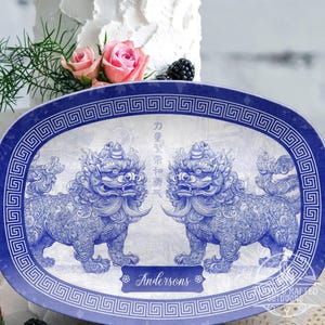 Pode incluir: Um prato oval de servir azul e branco com uma borda decorativa e dois cães foo azuis e brancos. O prato tem o texto "Andersons" no centro.