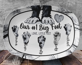 May include: White oval serving platter with a black and white illustration of a Bigfoot with the text "Our #1 Big Foot" and "LOVE, LITTLE FEET". Four footprints are shown with the names "Emma", "Liam", "Katy", and "Michael" written underneath.