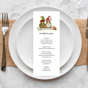 Op de afbeelding: Een kerstmenu met een feestelijke illustratie van twee kerstmannetjes op een slee. Het menu bevat voorgerecht-, hoofdgerecht- en dessert-opties. De tekst luidt: "menu", "voorgerecht", "Geitenkaassalade met lentegroenten en een rode peperdressing", "Groentesoep geserveerd met zuurdesembrood", "HOOFDGERECHT", "Kruidengebraden kalkoen met seizoensgroenten en een witte wijnjus", "Gepocheerde zalm met seizoensalade en aardappelen", "DESSERT", "Cheesecake Kersttaart"