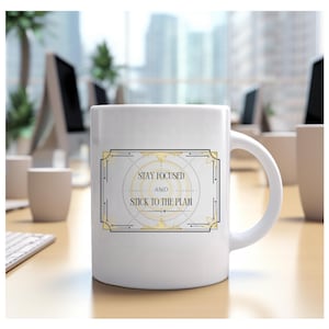 Könnte beinhalten: Weiße Keramiktasse mit einem gold-schwarzen Art-Deco-Design. Auf der Tasse steht der Text "Stay Focused and Stick to the Plan". Die Tasse hat einen gebogenen Henkel und wird wahrscheinlich für Heißgetränke verwendet.