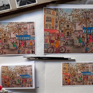 Puede incluir: Cuatro acuarelas que representan una escena de calle parisina con un caf&eacute;, tiendas y gente caminando. Las pinturas est&aacute;n enmarcadas y expuestas sobre un fondo blanco.