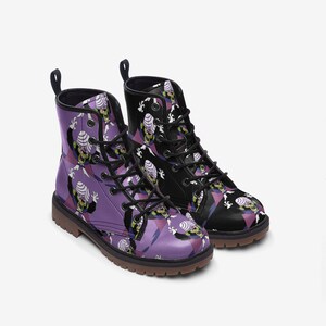 May include: Pair of combat boots with a cartoon character pattern. One boot is purple, the other is black. Both boots have black laces, pull tabs, and brown soles. The cartoon character has a green face, purple cape, and white hair.