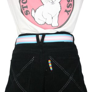 May include: Black corduroy pants with a white, blue, and pink striped belt. The pants have a rainbow-colored thread detail on the back pocket.