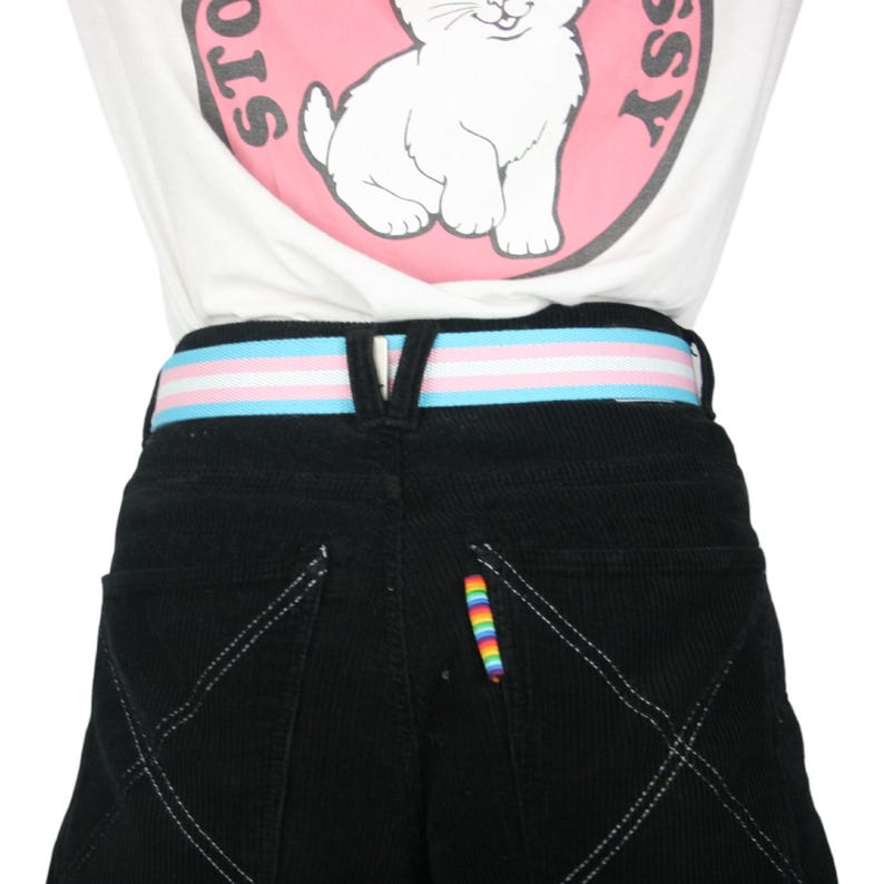 May include: Black corduroy pants with a white, blue, and pink striped belt. The pants have a rainbow-colored thread detail on the back pocket.