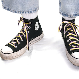 Könnte beinhalten: Ein Paar schwarze High-Top-Sneaker mit lila, gelben und weißen Schnürsenkeln. Die Sneaker sind abgenutzt und haben eine weiße Gummisohle.