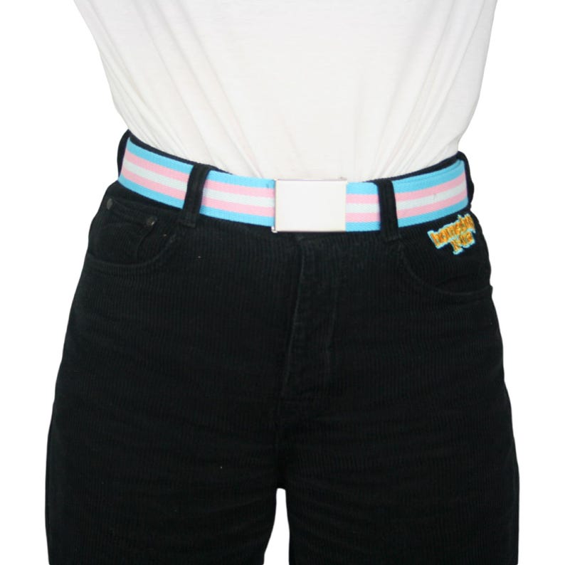 May include: A black corduroy pants with a white belt featuring blue and pink stripes. The belt has a silver buckle.