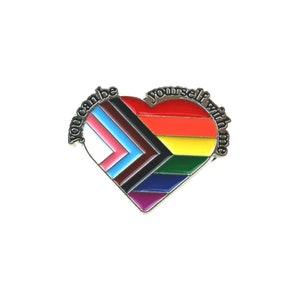 Könnte beinhalten: Eine herzförmige Emaille-Anstecknadel mit Regenbogen-Design und den Worten "You can be yourself with me". Die Anstecknadel zeigt die Farben der LGBTQ+-Pride-Flagge, der Transgender-Flagge und anderer Pride-Flaggen.