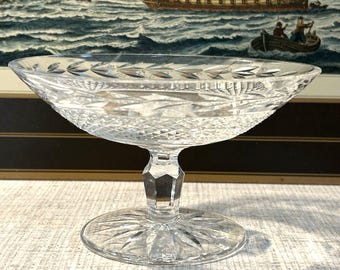 Peut inclure: Un bol sur pied en verre taillé transparent présentant un bord large avec un motif de feuilles, un corps à facettes en diamant, et une tige facettée reposant sur une base circulaire avec un motif en étoile. Le bol est transparent et lumineux.