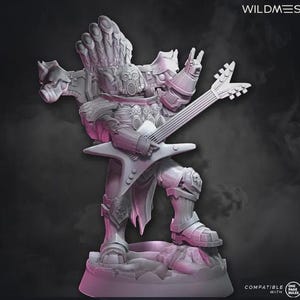 Peut inclure: Figurine grise imprimée en 3D d'un guerrier jouant de la guitare. Le guerrier porte une armure et un casque avec une crête en forme de mohawk. La guitare est en forme d'étoile. La figurine est sur un socle rocheux.
