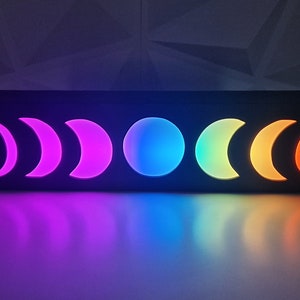 May include: A black wooden box with a rainbow moon phase design. The box is lit up with different colored lights, creating a colorful and whimsical effect.