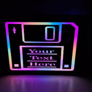May include: A glowing, stylized floppy disk icon with a rainbow gradient outline. The text "Your Text Here" is displayed in the center. The image is set against a black background, with a subtle reflection.