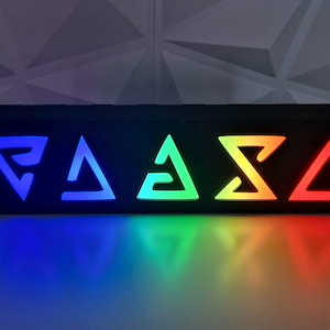 May include: A black rectangular box with five illuminated symbols, each a different color of the rainbow. The symbols are stylized triangles with a white outline.