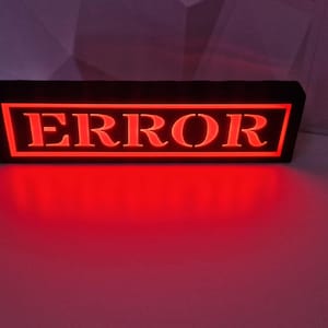 May include: A black rectangular sign with the word "ERROR" in white letters inside a red rectangle. The sign is illuminated with red LED lights.