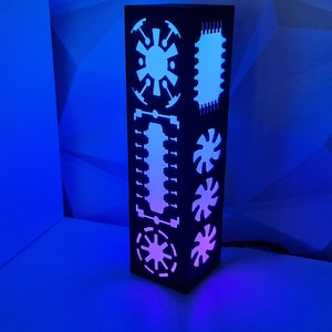 May include: A black lamp with a geometric design and white cutouts. The lamp is lit with a pink and blue light.