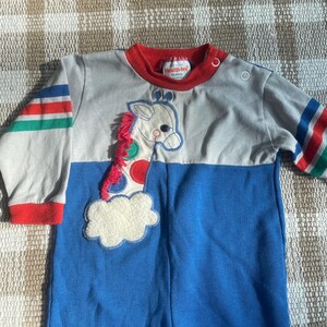 May include: A vintage baby one-piece outfit in blue, gray, and red. The outfit features a giraffe applique with a pink mane and colorful spots. The sleeves have striped accents, and the collar is red.