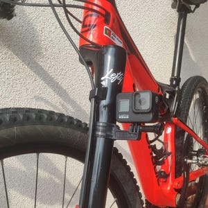 May include: A red mountain bike with a black front fork and a GoPro camera mounted on the fork. The bike has a black seat and black handlebars. The bike has a sticker on the frame that says "Lefty".