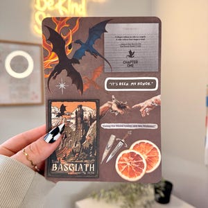 May include: A brown journal with dragon illustrations, text, and orange slices. The journal features the text "Read Books Be Kind", "Visit BASGIATH", and quotes like "It's been my honor." and "Going for blood today, are we, Violence?"