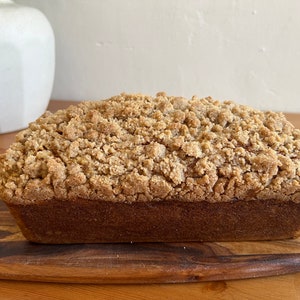 K&ouml;nnte beinhalten: Ein Brotlaib mit Streusel. Das Brot ist hellbraun und hat eine leicht goldene Kruste. Es liegt auf einem Holzbrett.
