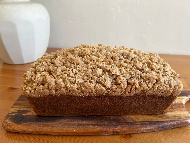 K&ouml;nnte beinhalten: Ein Brotlaib mit Streusel. Das Brot ist hellbraun und hat eine leicht goldene Kruste. Es liegt auf einem Holzbrett.