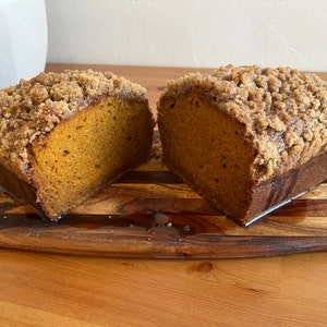 K&ouml;nnte beinhalten: Ein Laib K&uuml;rbisbrot mit Streusel-Topping, halbiert und auf einem Holzbrett pr&auml;sentiert.