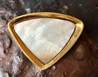 Könnte beinhalten: Eine dreieckige Schale mit goldfarbenem Rand und perlmuttweißem Innenraum. Die Schale hat eine glatte, reflektierende Oberfläche und einen goldenen Rand. Der Hintergrund ist eine dunkle, strukturierte Oberfläche.