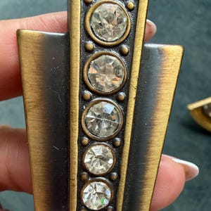 May include: Art Deco style metal hardware with a bronze finish. The hardware features a vertical row of five clear, round, faceted crystal accents. The edges are framed with a gold-tone metal.