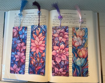 May include: Four floral design bookmarks with tassels. The bookmarks feature colorful illustrations of flowers in shades of pink, blue, and purple, resembling stained glass. Each bookmark has a different flower design.