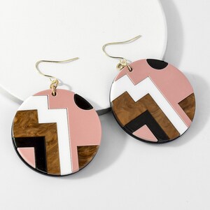 Pode incluir: Um par de brincos geométricos com padrão rosa, branco, marrom e preto com ganchos dourados.