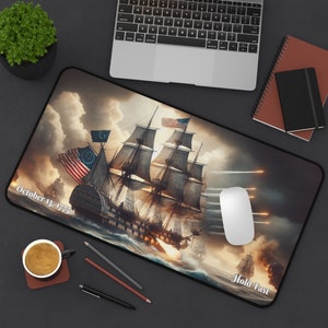 May include: A vintage-style mousepad featuring a dramatic scene of a ship battle with cannon fire and smoke. The ship has a large American flag and the text "October 13, 1775" and "Hold Fast" are visible.
