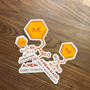 May include: Four white stickers with orange and red text and cartoon faces. The text on the stickers reads "A-MEAN-O ACID (SORRY I'M HAVING A BAD DAY)".