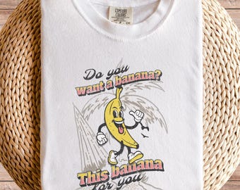 Peut inclure: T-shirt blanc avec un motif de banane de dessin animé et le texte "Do you want a banana? This banana for you".