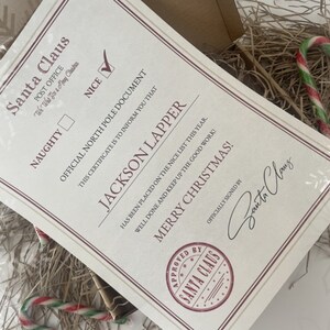May include: A Santa Claus "Nice" certificate with the name "Jackson Lapper" printed on it. The certificate is cream-colored with red and black text. The certificate is signed by Santa Claus and includes a candy cane.